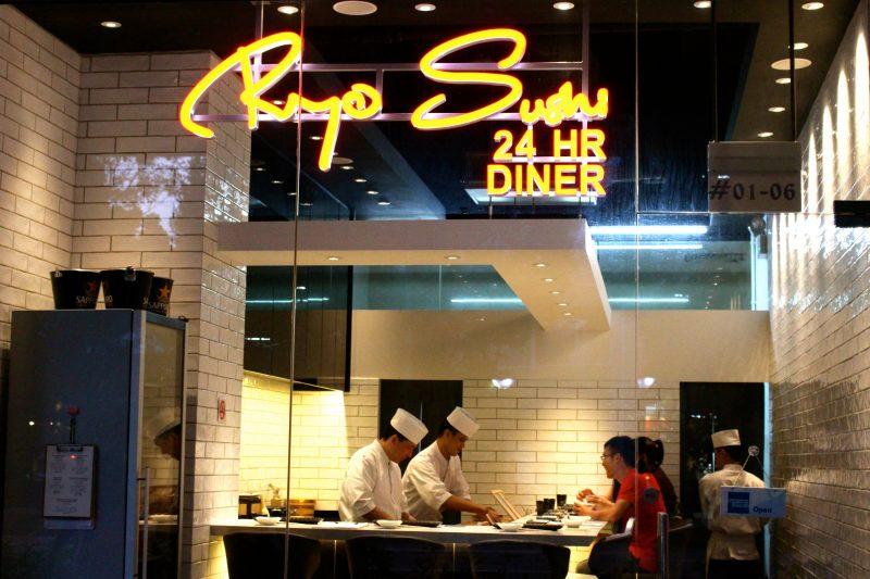 This image shows the glowing neon storefront of Ryo Sushi, a 24-hour diner with a modern, white-tiled interior.