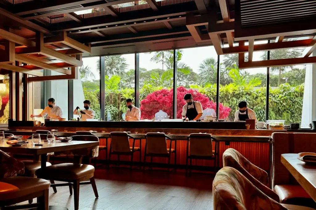 The sophisticated Omakase room at Wakuda Singapore, featuring chefs meticulously preparing seasonal dishes in a refined, intimate dining space overlooking lush greenery, embodying the harmony of world-class culinary art.