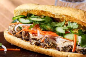 Close-up of a Vietnamese bánh mì sandwich filled with grilled pork, pickled carrots and daikon, fresh cucumber slices, jalapeños, and cilantro in a crispy baguette.