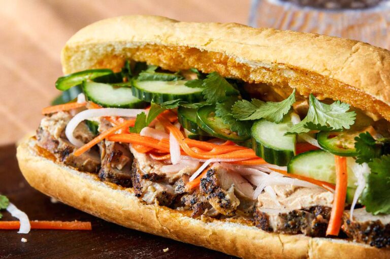 Close-up of a Vietnamese bánh mì sandwich filled with grilled pork, pickled carrots and daikon, fresh cucumber slices, jalapeños, and cilantro in a crispy baguette.