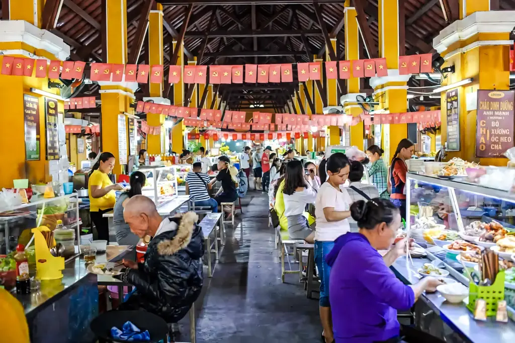 Interior of a Vietnamese food market with long counters, colorful banners, and diners enjoying local dishes.