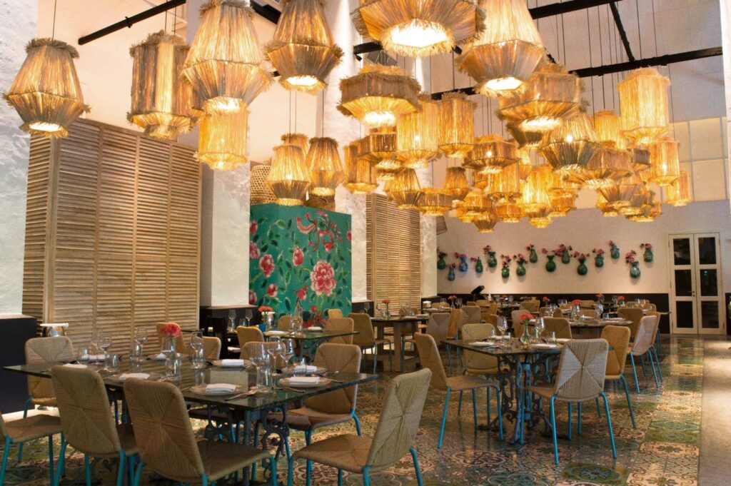 Candlenut Michelin‑starred Peranakan restaurant interior with rustic‑modern decor, hanging natural lights, floral wall art, teal vases, and patterned tiles.