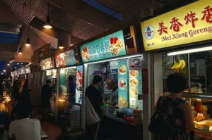Eye‑level wide‑angle shot of a Singapore hawker centre aisle lined with food stalls, illuminated signboards, and customers queuing for local dishes.