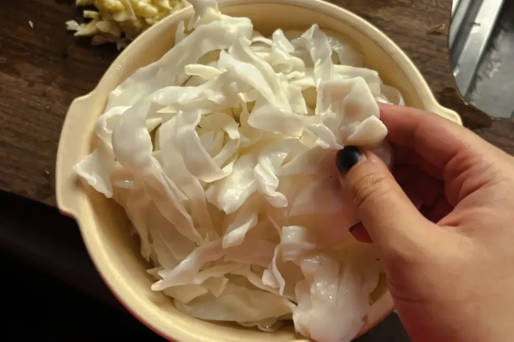 Overhead top‑down close‑up shot of raw flat rice noodles being separated by hand in a bowl, a key ingredient used for making char kway teow.