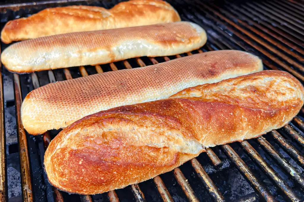 High-angle close-up of banh mi bread toasting on a metal grill, showing crisp, blistered crusts formed by high heat grilling used in Vietnamese street food preparation.
