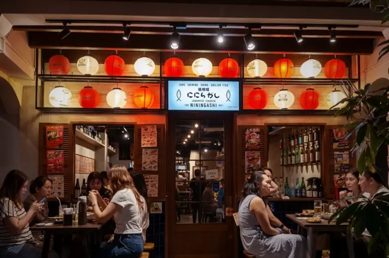 Cozy outdoor dining area at Niningashi Japanese Izakaya restaurant on East Coast, featuring patrons enjoying dinner under glowing red and white paper lanterns.