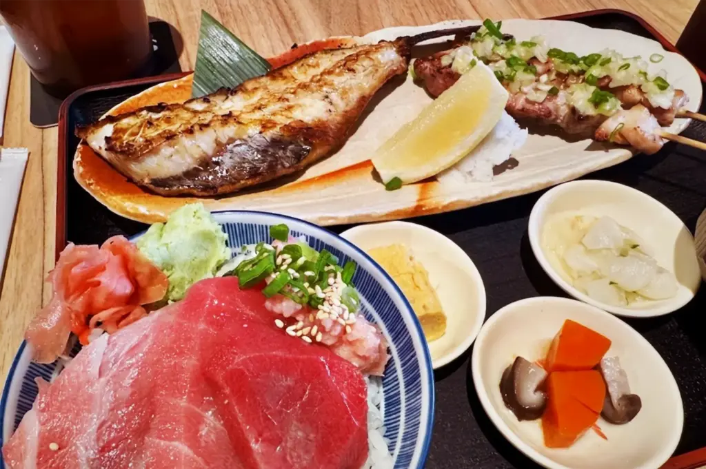 Authentic Japanese cuisine at Niningashi Izakaya, featuring a fresh Tuna rice bowl, grilled mackerel fish, yakitori skewers, and traditional side dishes.