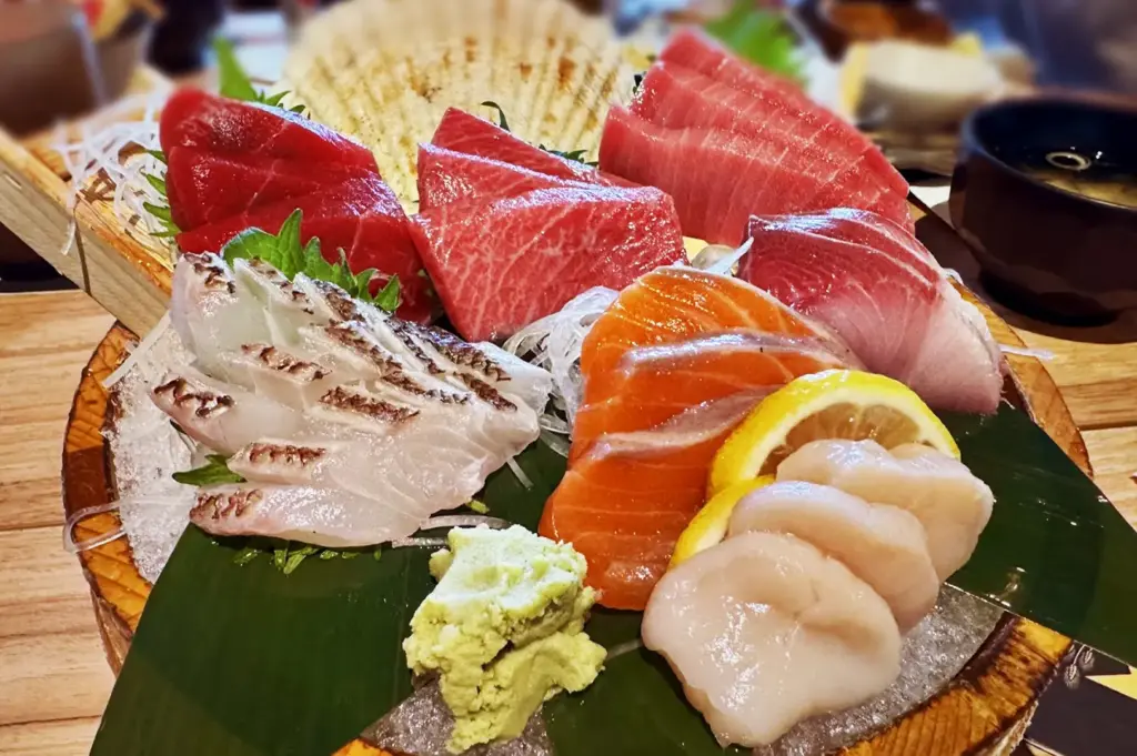 Fresh premium sashimi platter at Niningashi Japanese Izakaya, featuring slices of maguro tuna, sake salmon, hotate scallops, and white fish served with wasabi on ice.