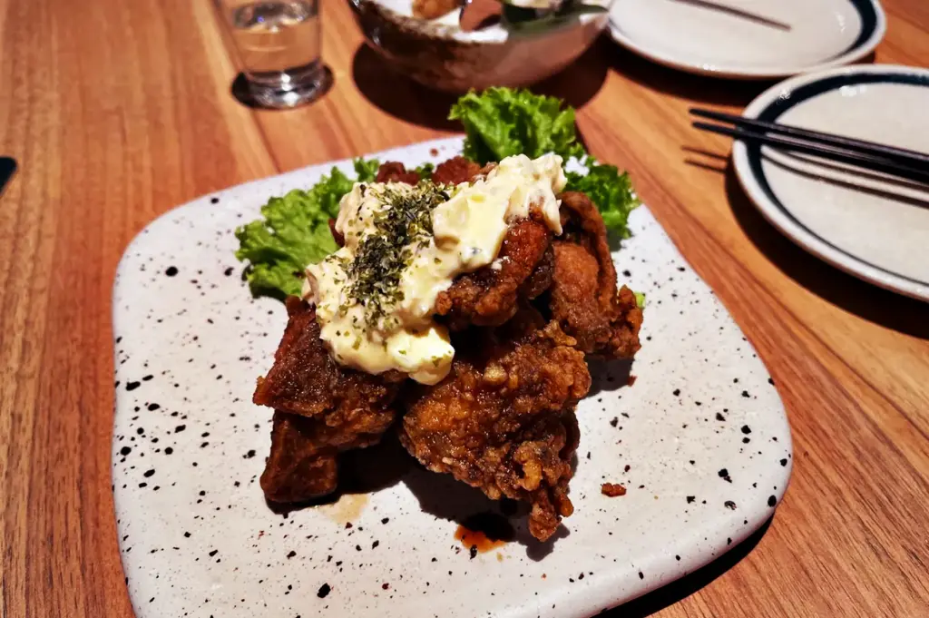 Crispy Chicken Nanban topped with creamy tartar sauce and chopped herbs, served over a bed of green lettuce at Niningashi Japanese Izakaya restaurant.