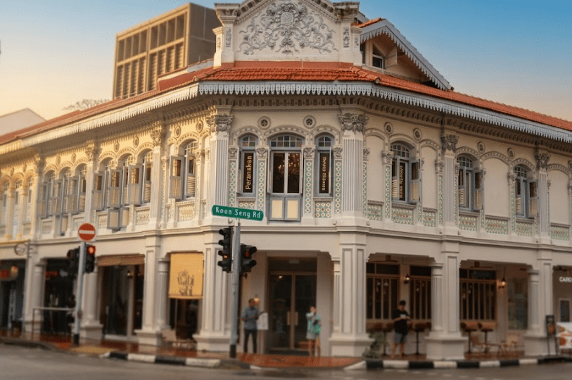 A beautiful, multi-story white heritage shophouse stands at the corner of Koon Seng Road in Singapore. The ground floor houses local eateries, showcasing the picturesque blend of traditional architecture and neighborhood dining of a japanese restaurant.