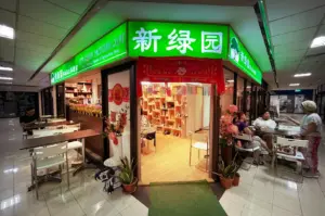 Entrance of New Green Pasture Cafe at Fortune Centre, Singapore, featuring a bright green signboard and outdoor seating.