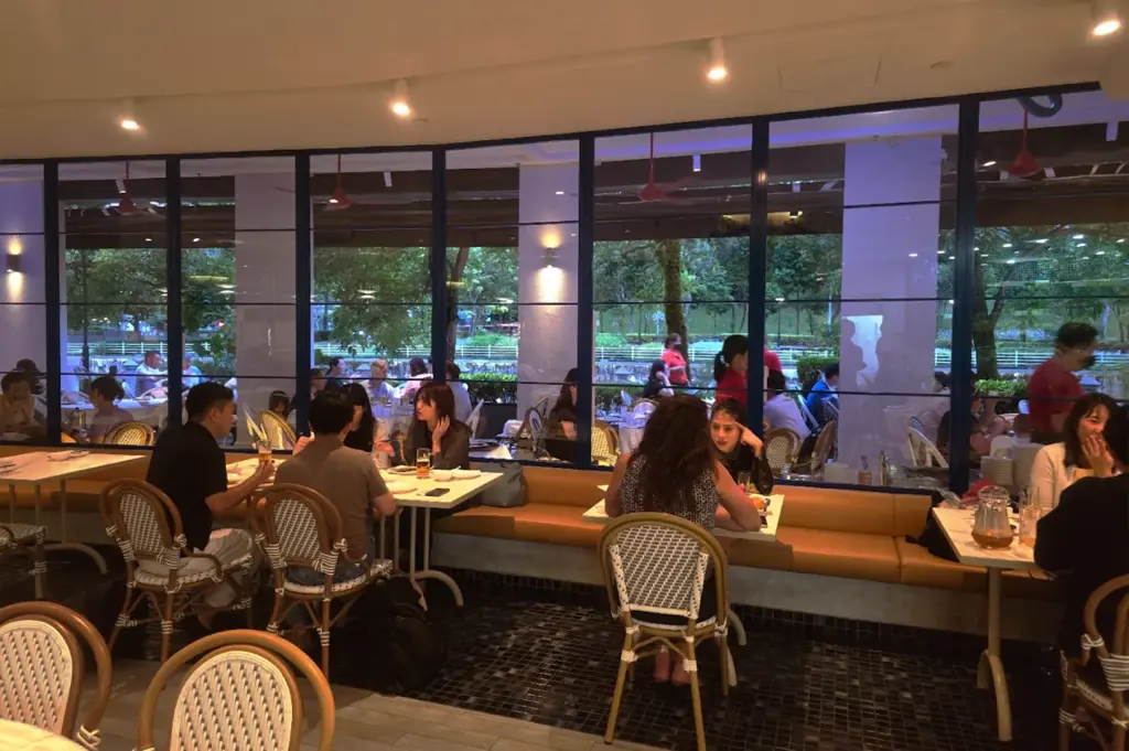 Guests dining inside the modern, glass-walled Long Beach Seafood restaurant with views of lush greenery, and the diners feeling right at home with comfortable seating to rest at their tables.