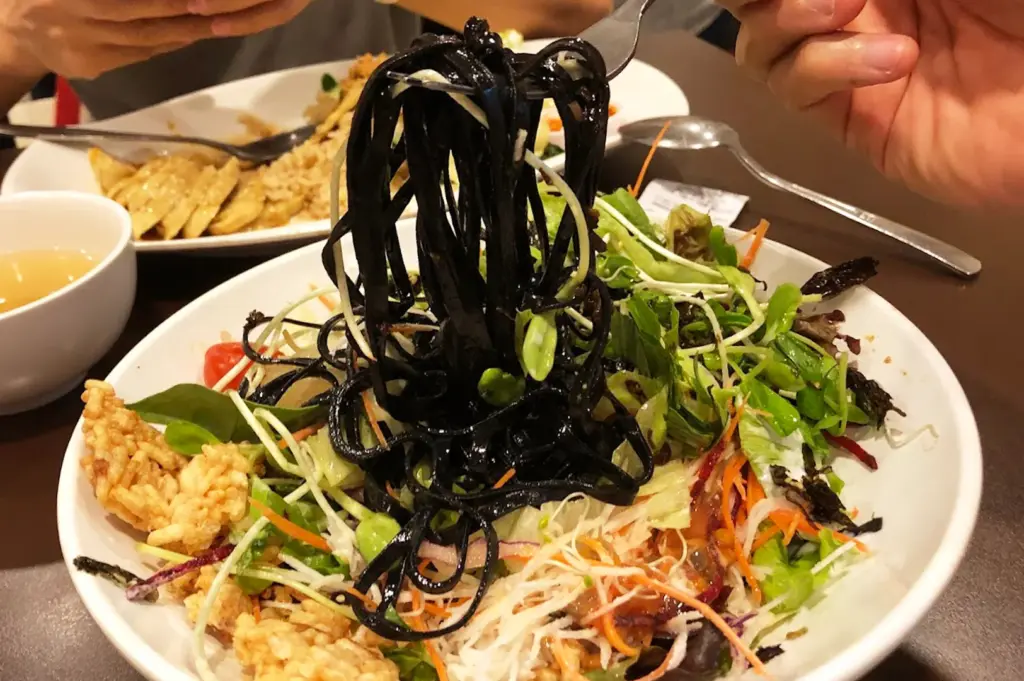 The signature Charcoal noodle salad at New Green Pasture Cafe, featuring black noodles, shredded purple cabbage and carrots, peanuts, and alfalfa sprouts.