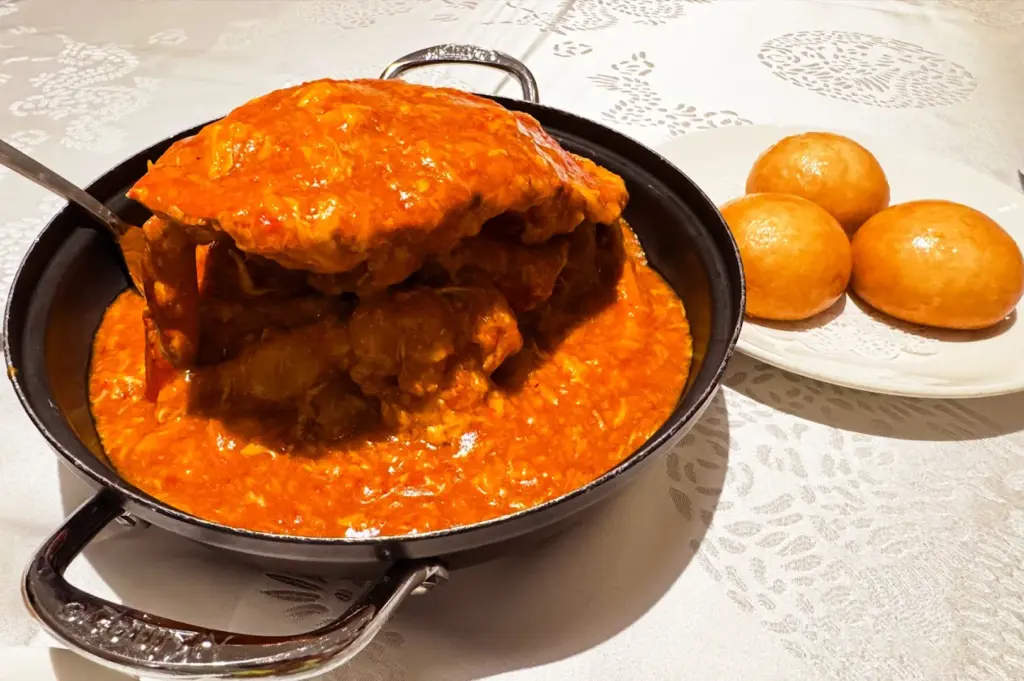 A delicious chili crab dish served in a pan with a side of crispy fried buns at Long Beach Seafood, a top destination for Singaporean seafood.