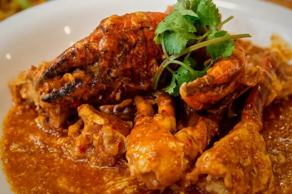 Close-up of Singapore chili crab served in a rich, savory tomato and chili gravy, garnished with fresh cilantro on a white plate.