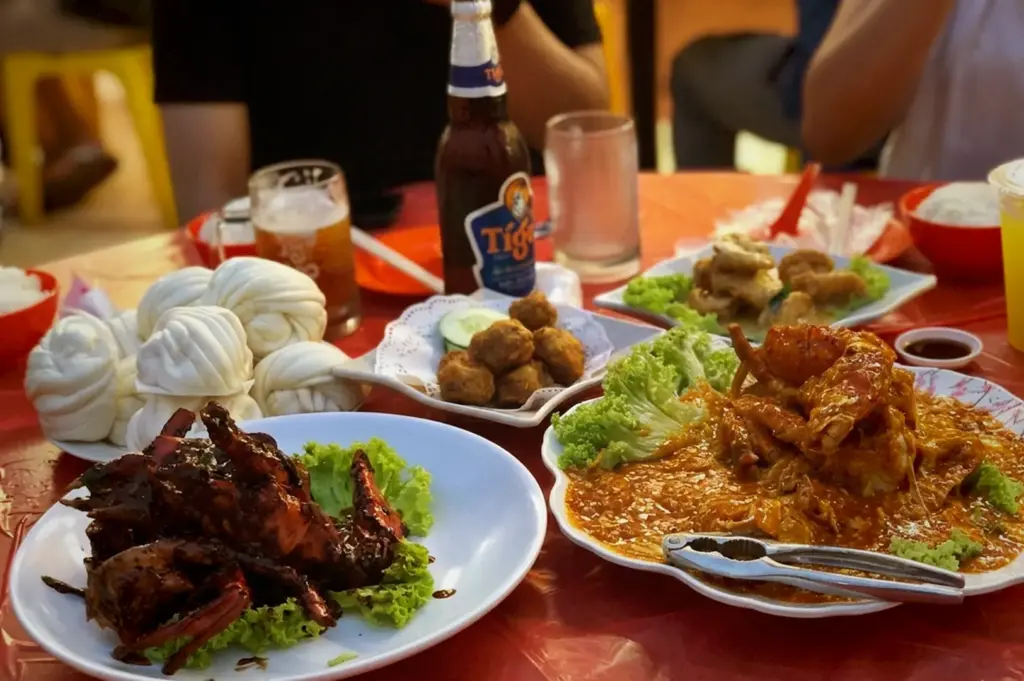 Family dining at Keng Eng Kee Seafood featuring chili crab, black pepper crab, steamed buns, and Tiger beer.