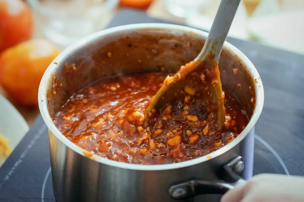 Close-up of a kitchen ladle to stir and thicken a rich, spicy, and savory chili sauce base in a pot to boil.