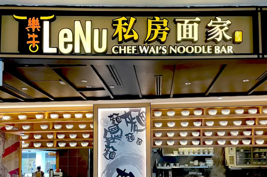 The modern, illuminated storefront signage of LeNu Chef Wai's Noodle Bar at VivoCity, featuring a decorative wall lined with ceramic bowls.