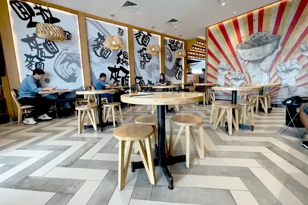 The interior dining space of LeNu Chef Wai's Noodle Bar, showcasing stylish wooden furniture, minimalist decor, and artistic wall murals in a comfortable, contemporary setting.