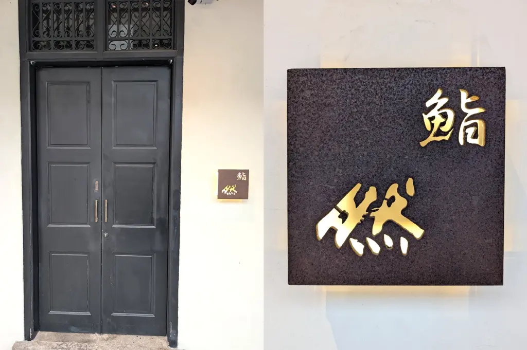 Exterior entrance and signage of Sushi Zen in Singapore, featuring elegant Japanese calligraphy on a stone plaque, marking the destination for a premium Omakase dining experience.