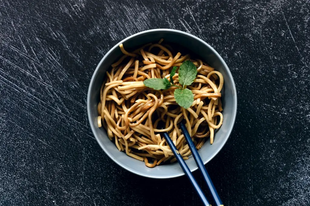 A simple, elegant bowl of wheat-based Chinese noodles garnished with fresh mint, highlighting the versatility of the wheat noodle family.