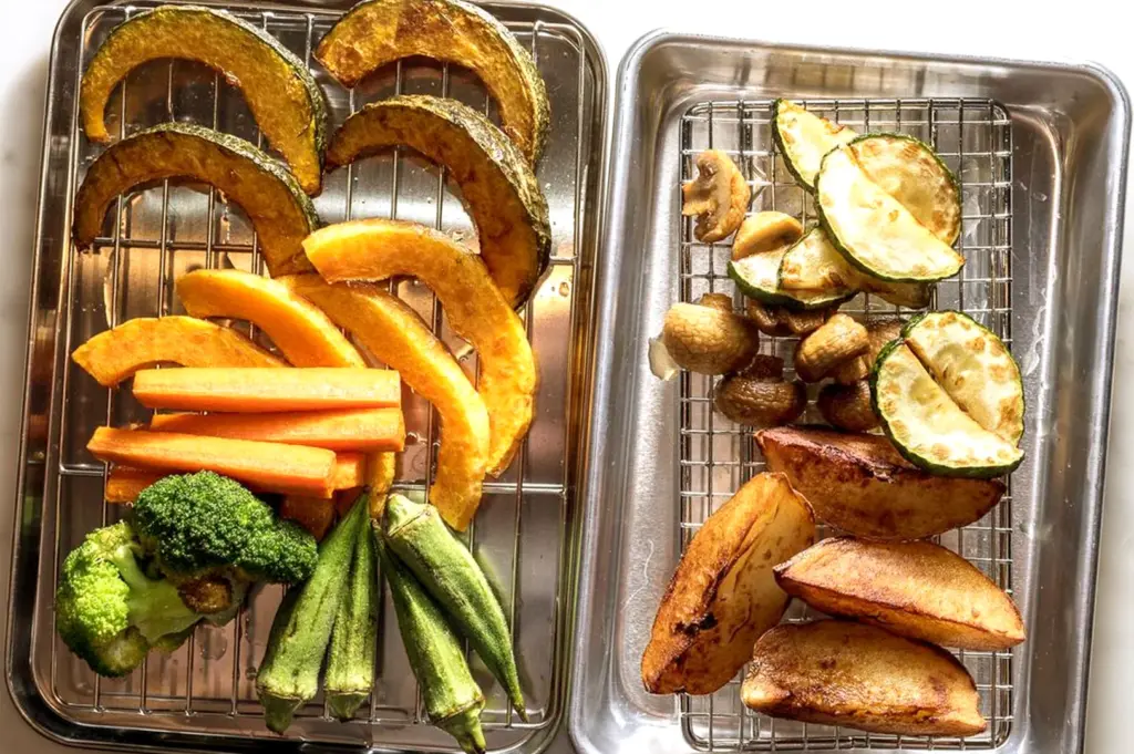 A culinary preparation shot showing two metal trays of perfectly roasted, colorful vegetables, including pumpkin, carrots, broccoli, okra, zucchini, and potatoes, ready to be added to authentic Japanese soup curry.