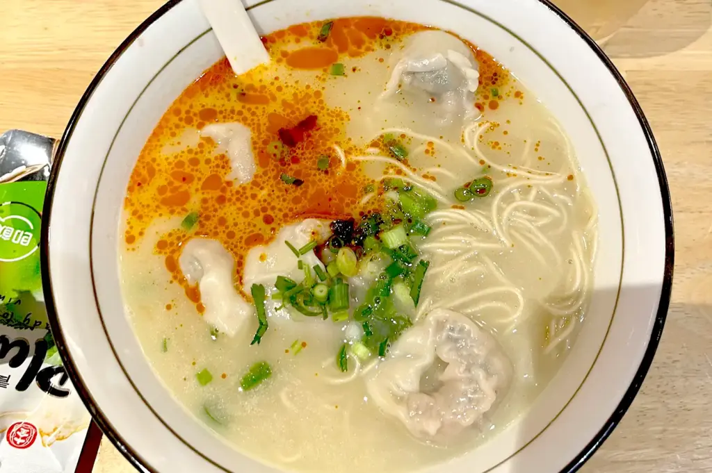 A bowl of tomato pork bone broth noodle soup from LeNu Chef Wai's Noodle Bar, highlighting the rich, creamy broth, tomato flavors, and tender pork dumplings.