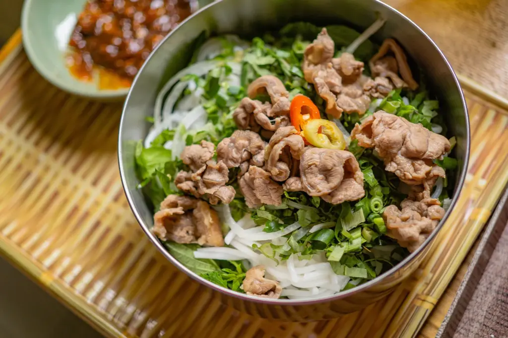 A bowl of fresh, flat rice noodles from the rice family served with tender meat and aromatic herbs, emphasizing the soft and smooth nature of rice-based Chinese cuisine.
