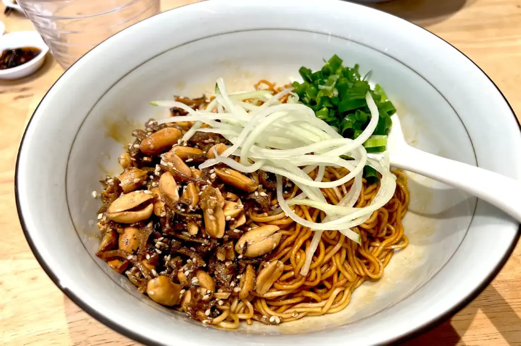 A colorful, dry-tossed noodle dish at LeNu Chef Wai's Noodle Bar, garnished with roasted peanuts, shredded cucumber, and fresh scallions for a balanced texture and flavor.