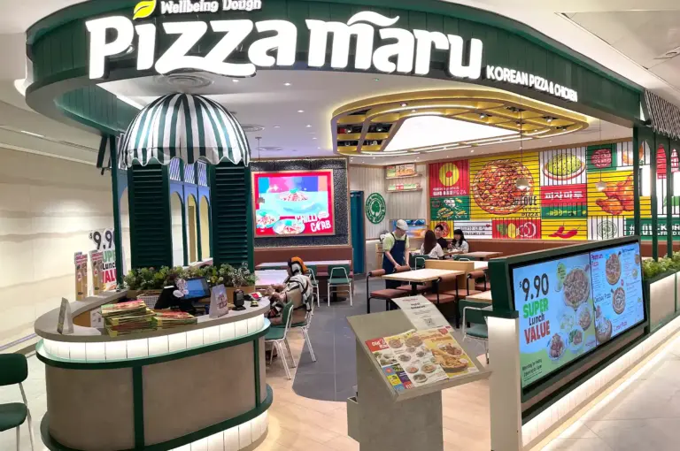 The bright green and wood-themed storefront of Pizza Maru, a popular Korean pizza and chicken restaurant in Singapore, showcasing indoor dining areas and a menu board.