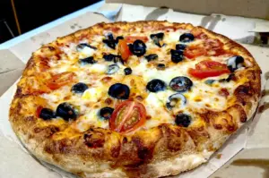 Freshly baked classic pizza in a cardboard delivery box from a popular Singapore pizzeria featuring melted cheese, cherry tomatoes, and black olives.