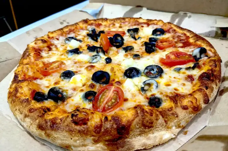 Freshly baked classic pizza in a cardboard delivery box from a popular Singapore pizzeria featuring melted cheese, cherry tomatoes, and black olives.