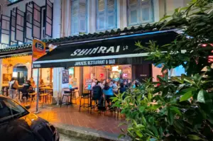 The street-facing storefront of Shinrai Japanese Restaurant & Bar in Singapore, featuring a black awning, outdoor dining tables, and lively evening ambiance.