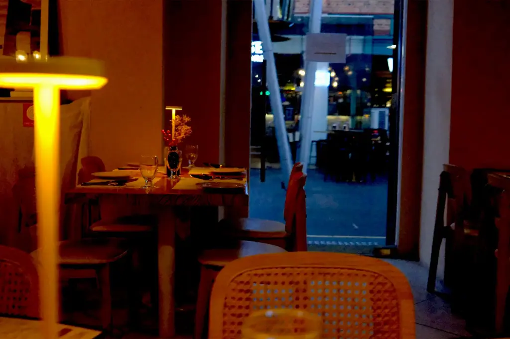 An intimate restaurant interior with warm, low lighting, cozy wooden tables, and a glowing table lamp, creating a slow-down atmosphere ideal for meaningful conversations.
