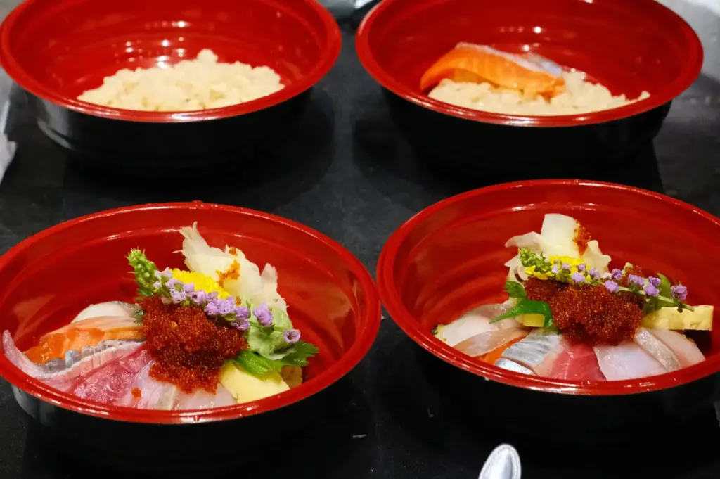 A step-by-step assembly of chirashi bowls at Araya Shouten, showing red lacquer bowls filled with seasoned sushi rice topped with fresh salmon slices, sashimi cuts, tobiko roe, and edible flower garnishes.