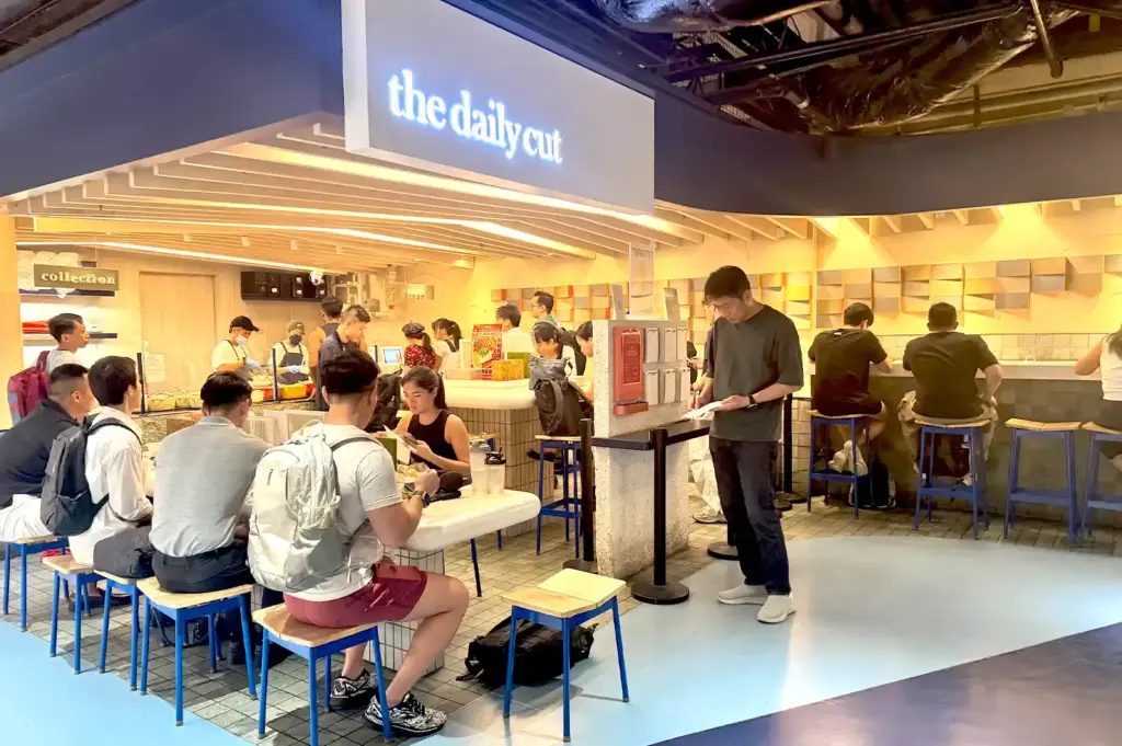 The Daily Cut at One Raffles Place filled with office workers during the busy lunch rush, showcasing its popular customizable protein bowl counter and seating area.
