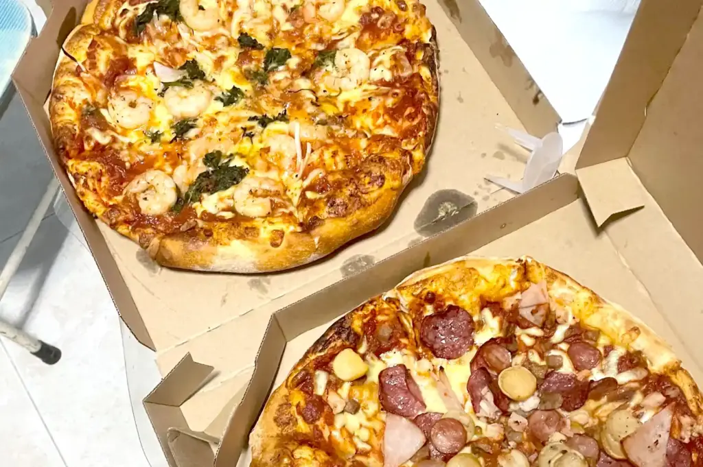 Domino's Pizza delivery boxes containing seafood and meat pizzas loaded with prawns, cheese, and sliced sausages in Singapore.