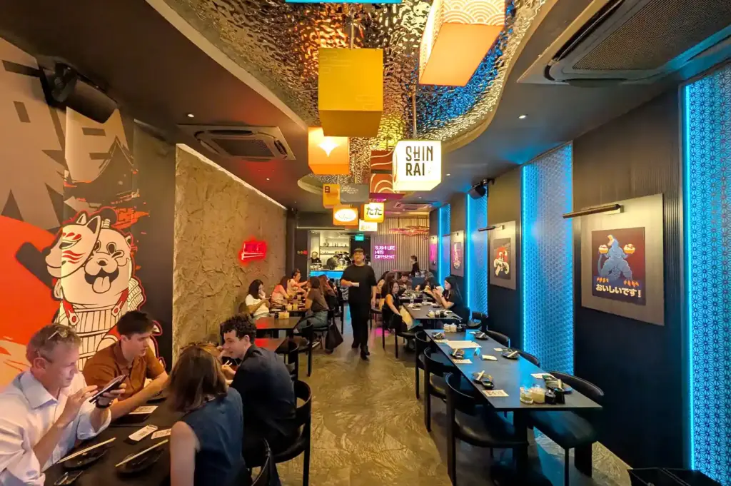 The vibrant interior dining space of Shinrai featuring modern cube lanterns, stylish wall art, and cozy table seating filled with diners.