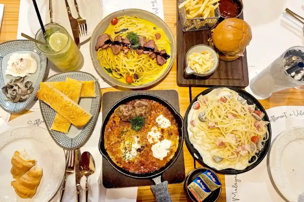 A top-down view of a lavish dinner spread featuring gourmet pasta dishes, a cast-iron skillet meal, toasted bread, a burger, and refreshing drinks for a memorable dining experience.