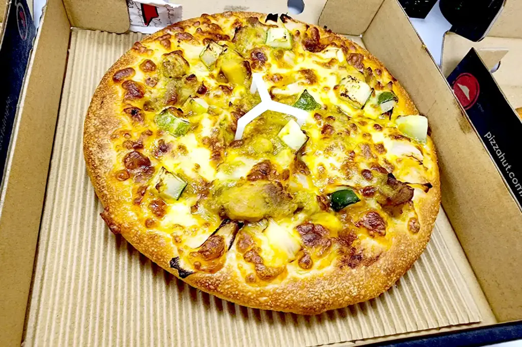 Pizza Hut Singapore delivery pizza box showcasing a fusion Asian curry-flavored crust topped with chicken satay chunks and vegetables.