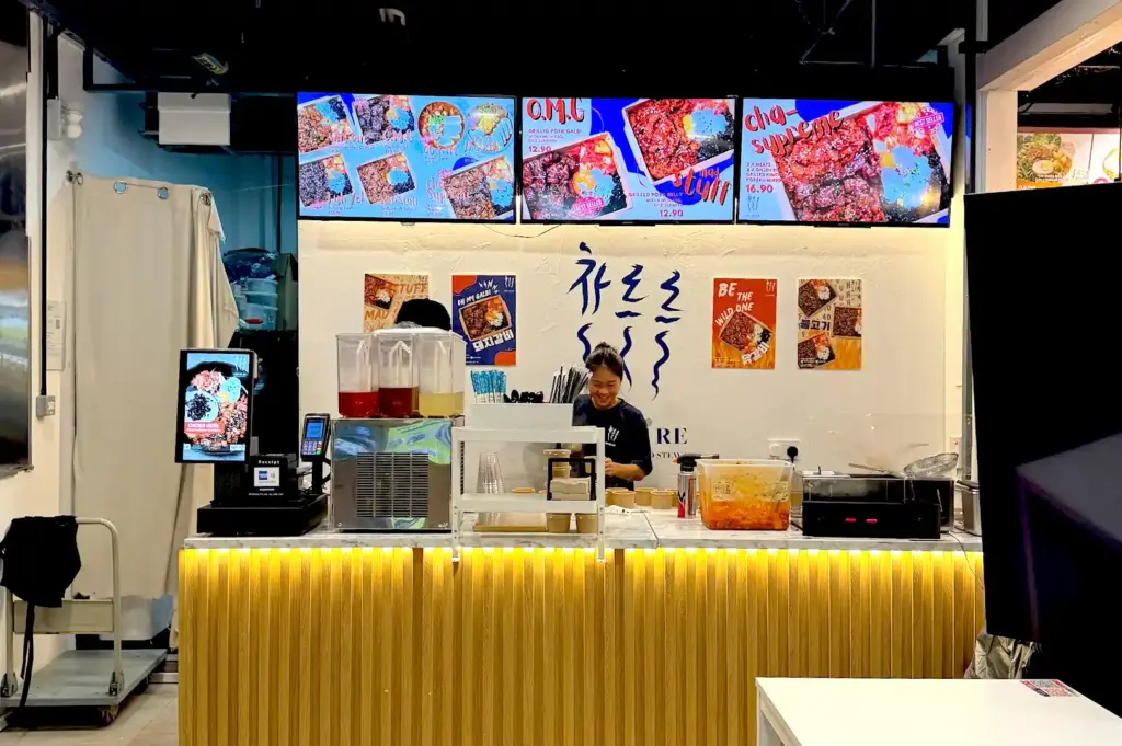 The vibrant storefront of Che Re Re at One Raffles Place, highlighting digital menu boards displaying Korean grilled pork bowls and quick lunch options.