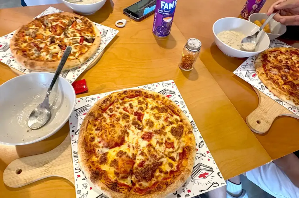 Canadian Pizza Singapore delivery spread featuring hearty meat-topped pizzas, creamy soup bowls, and soft drinks on a wooden dining table.