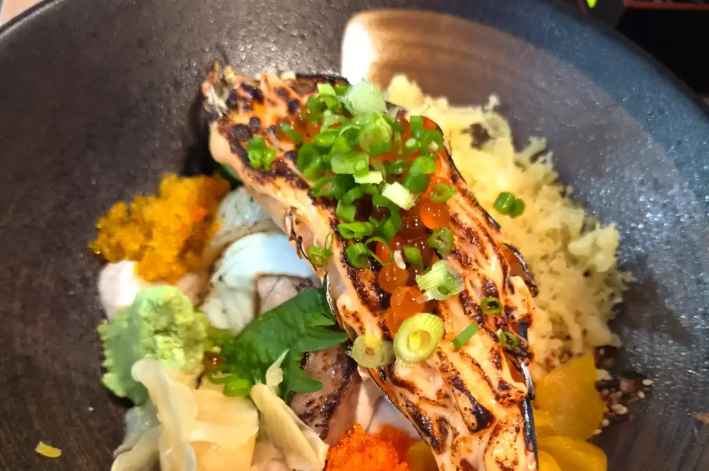 A bowl of aburi chirashi don from Age Ya at Far East Plaza topped with seared salmon, mentaiko sauce, ikura, tobiko, crispy tenkasu flakes, and pickled ginger over rice.