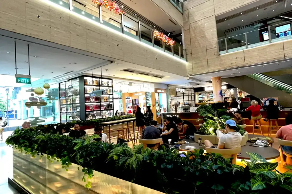 A vibrant, open-concept dining area inside One Raffles Place, featuring lush greenery, contemporary seating, and diverse food options to help the lunchtime crowd quickly decide where to eat in the Singapore CBD.