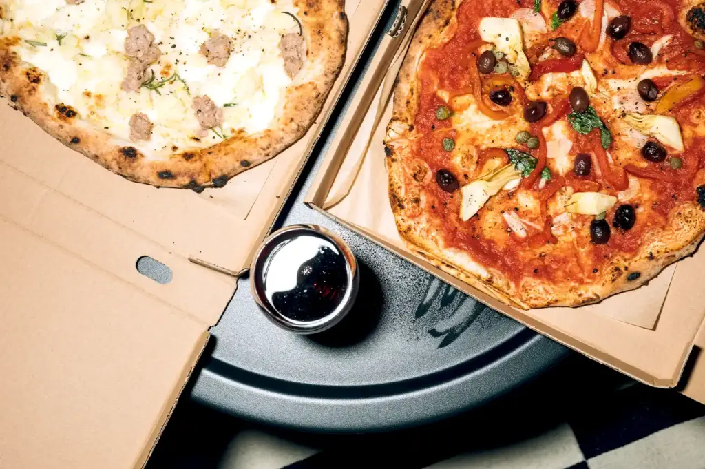 Wood-fired gourmet pizza delivery boxes from a top Singapore pizza spot showcasing artisan crusts with fresh artichokes, olives, and sausage.