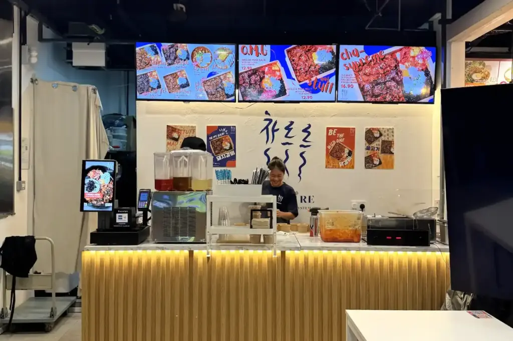 The vibrant storefront of Che Re Re at One Raffles Place, highlighting digital menu boards displaying Korean grilled pork bowls and quick lunch options.