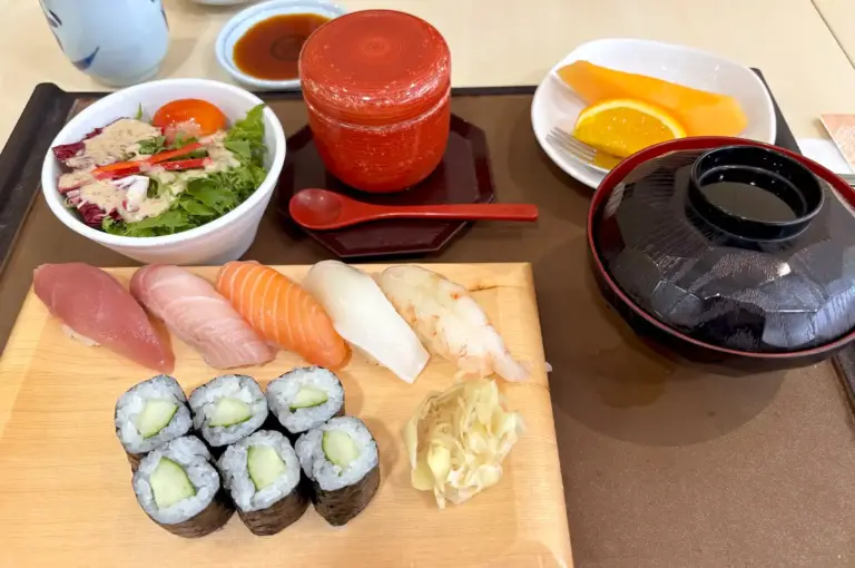 A fresh sushi platter featuring assorted nigiri, cucumber maki rolls, a side salad, miso soup, and fresh fruit.