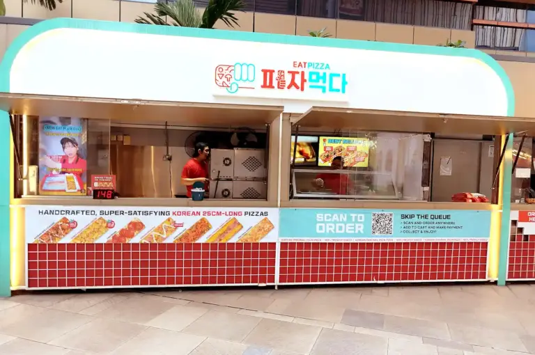 The vibrant storefront of Eat Pizza at Paya Lebar Quarter (PLQ), showcasing its turquoise and white exterior, Korean signage, and promotional displays for handcrafted 25cm-long pizzas.