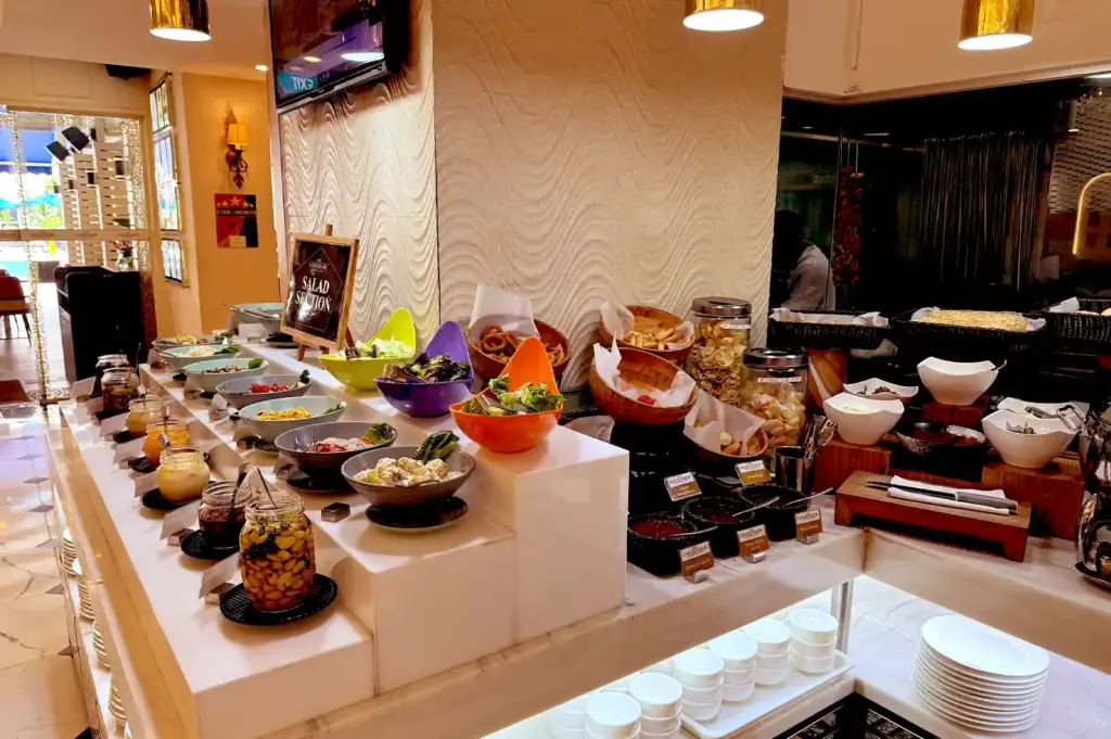 A vibrant salad station at a halal buffet offering colorful bowls of greens, dressings, sliced vegetables, crackers, and neatly stacked white plates.