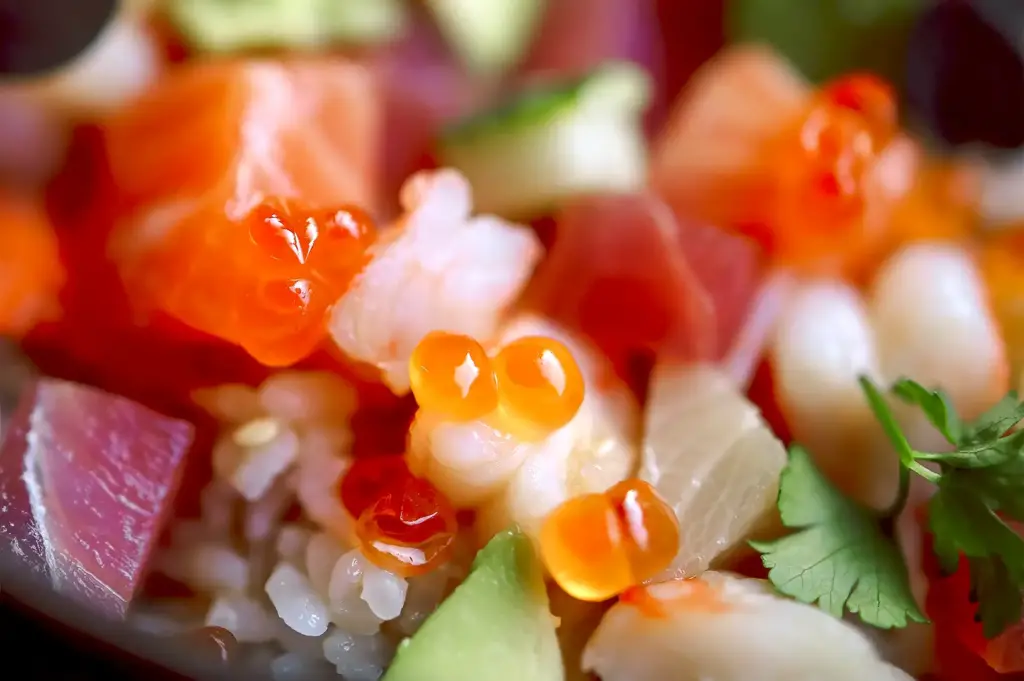 Close-up view of fresh Chirashi toppings including glossy salmon roe, diced tuna, tender shrimp, and crisp cucumber chunks.
